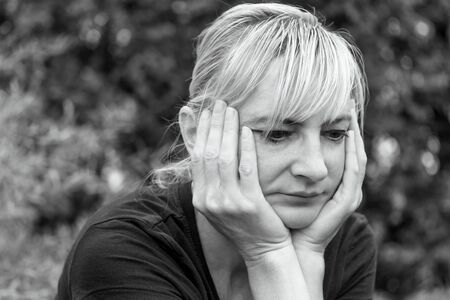 Side monochrome portrait of a frustrated middle aged woman, who is supporting her face by hands and is looking ahead.の写真素材