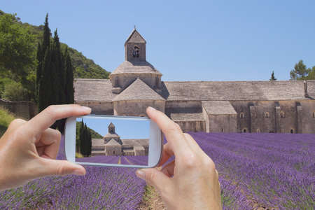 In the bottom left of the photo are hands holding smart phone, whose screen contains photo of the Senanque Abbey.  Background of the photo contains also the Senanque Abbey (Provence, France)の写真素材