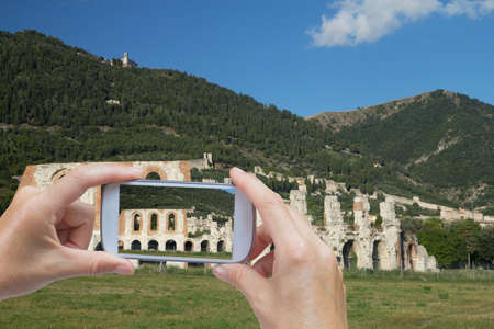 In the bottom left of the photo are hands holding smart phone, whose screen contains photo of Gubbio.  Background of the photo contains also historic town of Gubbio (Italy)の写真素材
