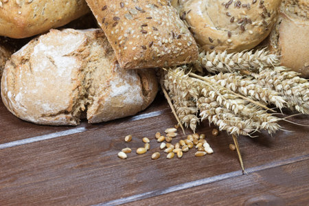 Wholemeal bread and pastries are lying on a wooden table at the top of the picture. Ears and grain...