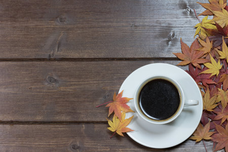 Aerial view of white cup of coffee with color maple leaves on a wooden table.の写真素材