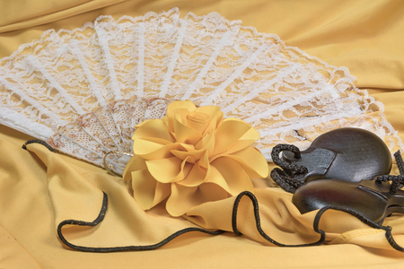Closeup view of black castanets, yellow rose and white fan lying on a yellow clothing for Flamenco dance.の写真素材