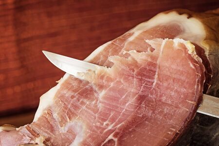 Cutting a slice of Spanish ham by knife. Photo is edited as a vintage with dark edges. Horizontally.の写真素材