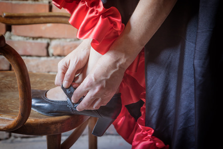 Closeup view of a Flamenco dancer with her foot on an old wooden chair and putting on the black old shoe. The photo has deliberately darkened edgesの写真素材