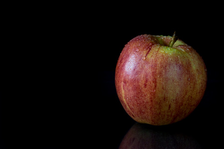 Low key picture of reflecting red apple with water drops on a black background.の写真素材