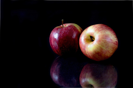 Low key picture of two reflecting red apples on a black background.の写真素材