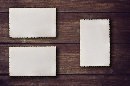 Blank vintage photos with jagged edges are lying on the brown wooden desk. Two horizontally and one...