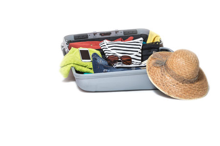 Studio shot of a suitcase packed with clothes, sunglasses, shirts, straw hat and a smart phone....