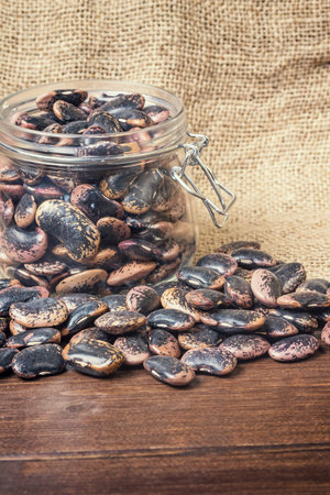 Beans spilled around the glass on burlap and wooden desk. Edited as a vintage photo. Vertically.  