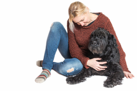 Studio shot of blond middle aged woman sitting with the Giant Black Schnauzer dog on the white background. The womnan is looking at the dog.の写真素材