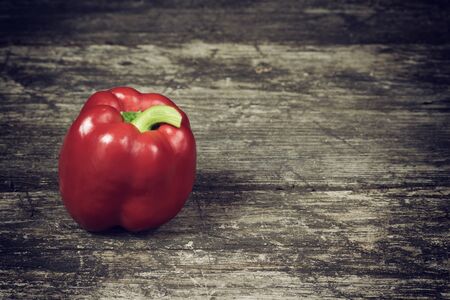 Red pepper standing alone on an old wooden table. Edited as a vintage photo with dark edges.の写真素材