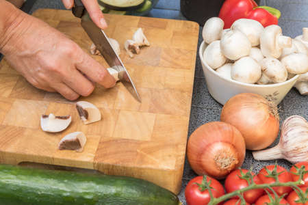 Side view of woman slicing a mushrooms on a wooden board. Various types of vegetables are lying on the table.の写真素材