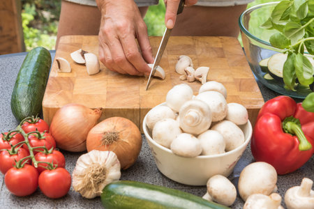 Front view of slicing a mushrooms on a wooden board. Various types of vegetables are lying on the...