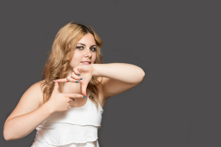 Portrait of smiling attractive long haired young woman showing gesture camera. All is on the gray background. の写真素材