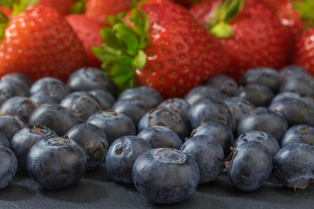 Mix of strawberries and blueberries lying on a dark stone table. Focused on the blueberries in the foreground.の写真素材