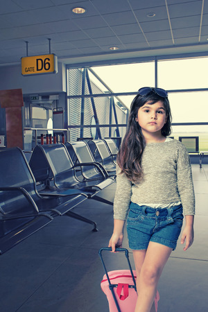 Long haired little girl with a pink suitcase is standing in an empty airport hall.の写真素材