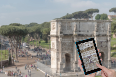Female finger touching tablet with detail of Arch of Constantine in Rome (Italy). Intentionally blurred image of the Arch of Constantine is in the background. All potential trademarks are removed.の写真素材