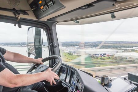 View of truck driver in interior of truck cabin.The truck crosses the Queen Elizabeth II Bridge over the Thames near London.の写真素材