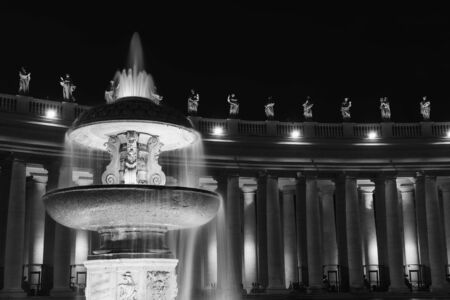 Black and white photo of fountain in front of Colonnade at St. Peter's Square in Vatican at night.の写真素材