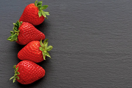 Strawberries forming a row on the left side of the photo. All on a dark slate desk. There is enough...