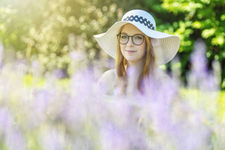 Portrait of smiling young woman with glasses wearing white  summer hat is posing behind lavender in the gardenの写真素材
