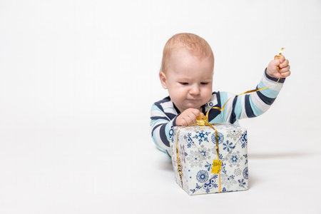 Little toddler boy is untying  Christmas package lying on the floor. All is on the white background
