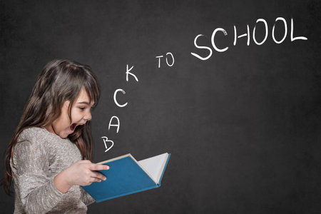 Cute tanned long haired  little girl is surprised at the letters Back to School coming out of an...
