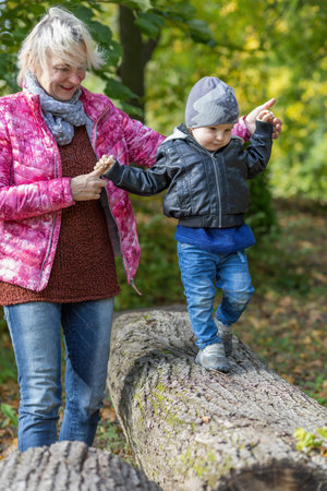 Young grandmother with her little grandson are playing together in autumn park