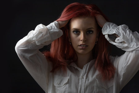 Low key portrait of beautiful redhead  young woman with both hands in her hair. Horizontally.