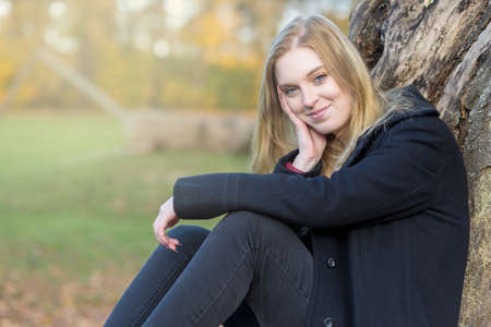 Portrait of smiling girl sitting in autumn park. The girl is looking at the camera.の写真素材