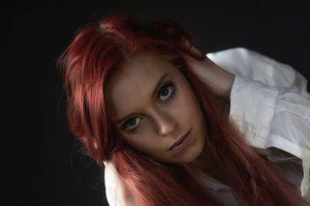 Low key closeup portrait of  redhead young woman in trouble looking at the camera.  Horizontally.の写真素材