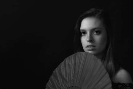 Low key black and white portrait of beautiful young woman holding  the fan. Horizontally.の写真素材