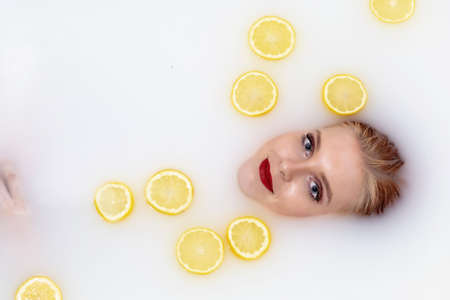 Attractive young  woman with red lips takes a bath with milk and citrus fruits. Horizontally.の写真素材