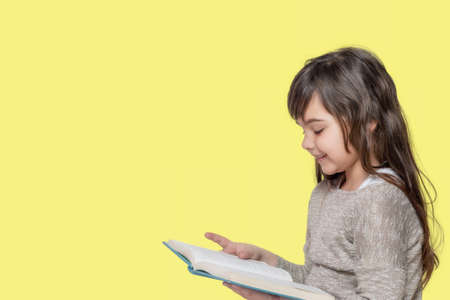 Cute tanned little girl is reading book on the yellow background ready for your text.の写真素材