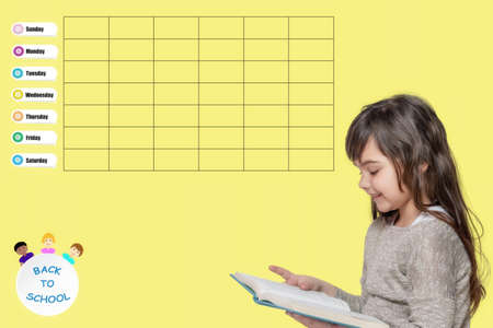 Cute tanned little girl is reading book. The  school weekly planner is on the yellow background. Sunday starts week.の写真素材
