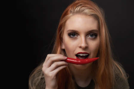 Low key portrait of beautiful long hair young woman posing with fresh chili pepper looking at the camera.の写真素材