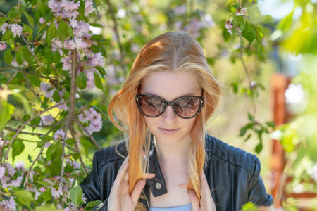 Attractive long hair girl with glasses is posing in front of blooming sakura tree.Horizontally.
