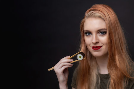Portrait of attractive  long hair young woman tasting sushi by wooden sticks  looking at the camera....