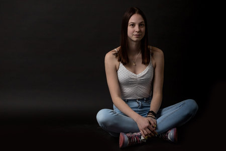 Portrait of young woman sitting on black background. Horizontally.