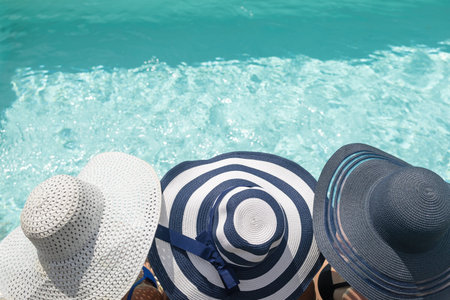Top view of head of three women wearing straw hat sitting on the edge of the swimming pool. Horizontally.の写真素材