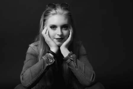 Black and white portrait of smiling attractive young woman with sunglasses on her head is sitting on the black background. Horizontally.の写真素材