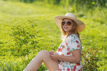 Portrait of attractive  young woman in straw hat sitting outdoors in summer day. Horizontally.の写真素材