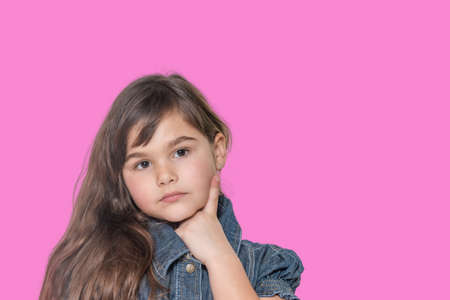 Cool tanned long haired little girl wears  denim costume is posing on pink background.の写真素材