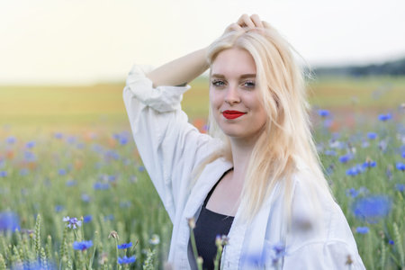 Smiling attractive blonde woman with hand in hair in cornflower and poppy meadow. Horizontally.の写真素材