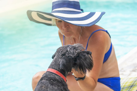 Woman wearing summer straw hat is posing with black schnauzer dog by the pool. Horizontally.の写真素材
