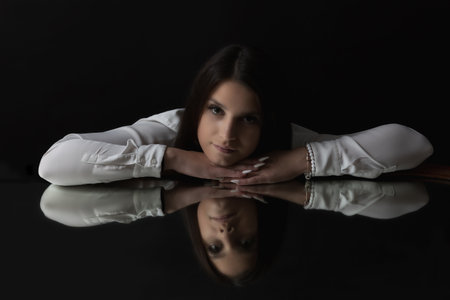 Low key portrait of brunette young woman  lying on the mirror and looking at the camera. Horizontally.の写真素材