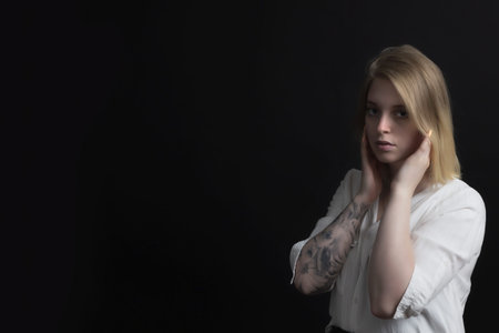 Low key portrait of blonde sad young woman weared in white shirt with tattoo on her hand.の写真素材