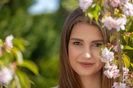 Attractive brunette girl posing near sprig of cherry blossoms. Horizontally.の写真素材