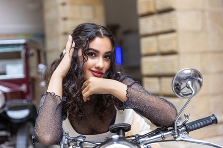Portrait of  sexy tanned girl sitting on a vintage motorcycle with  hand in her hair.  Horizontally.の写真素材