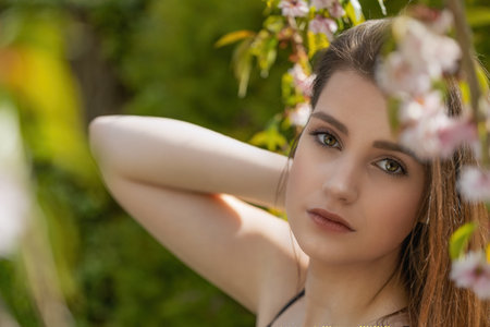 Cool brunette girl is posing on camera outdoors near sakura tree closeup.  Horizontally.の写真素材